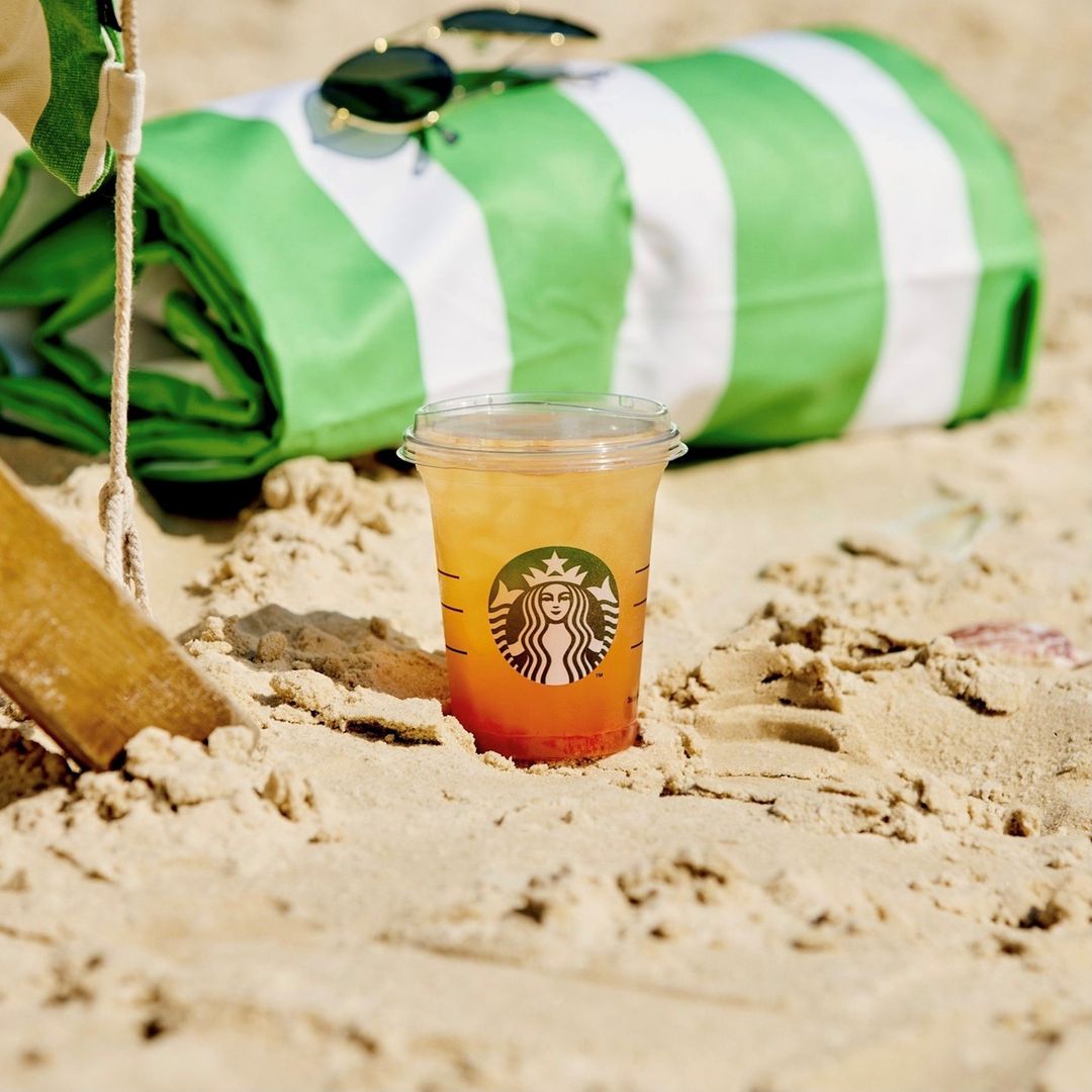 A Strawberry Sunset drink from Starbucks in a cup on some sand